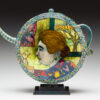 A teapot with a painting of a woman 's face on it.