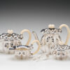 A group of tea pots and cups with spoons.
