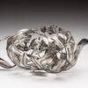 A silver bowl with leaves and branches on it.