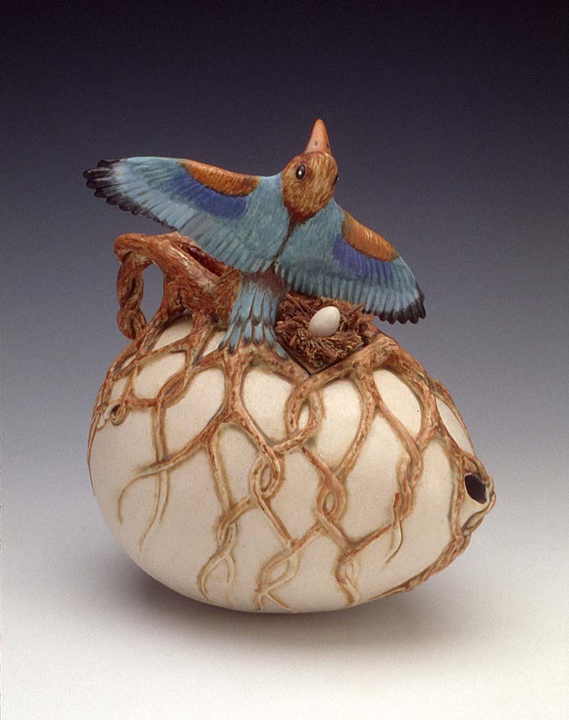 Kathryn McBride, "Roots and Wings" 1993. A ceramic egg with overlay of tree roots, topped with a blue bird with spread wings.