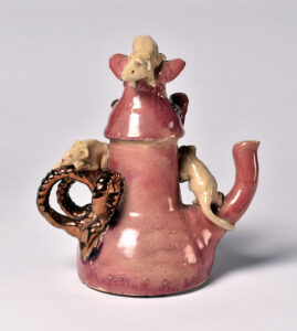 A pink teapot with a dragon handle on top of it.
